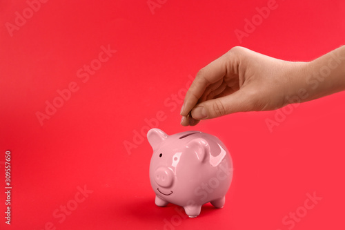 Woman putting coin into piggy bank on red background, closeup. Space for text