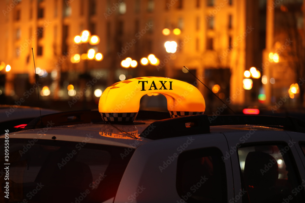Fototapeta premium Taxi car with yellow checkered sign on city street in evening, closeup
