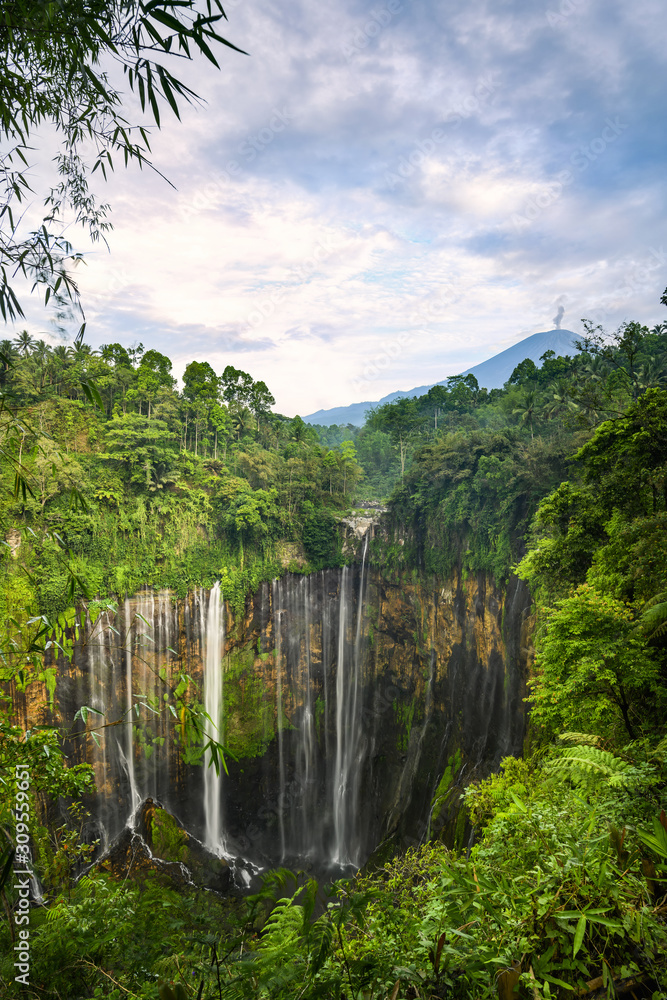 View from above, stunning aerial view of the Tumpak Sewu Waterfalls also known as Coban Sewu with the Semeru volcano in the distance, Malang Regency,East Java, Indonesia.