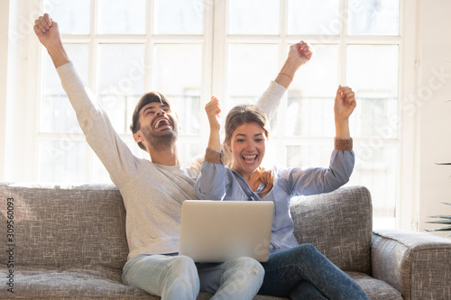 Happy young couple celebrate online victory, using laptop together photo