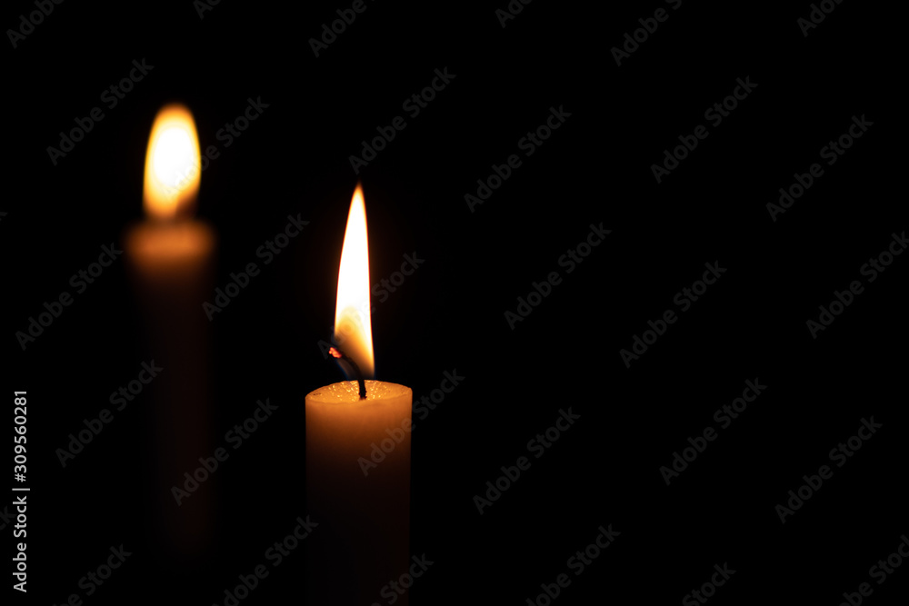 Two isolated burning yellow candles on a black background. The flame of two orange wax candles in the dark Two isolated burning yellow candles on a black background. The flame of two orange wax candles in the dark