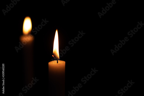 Two isolated burning yellow candles on a black background. The flame of two orange wax candles in the dark