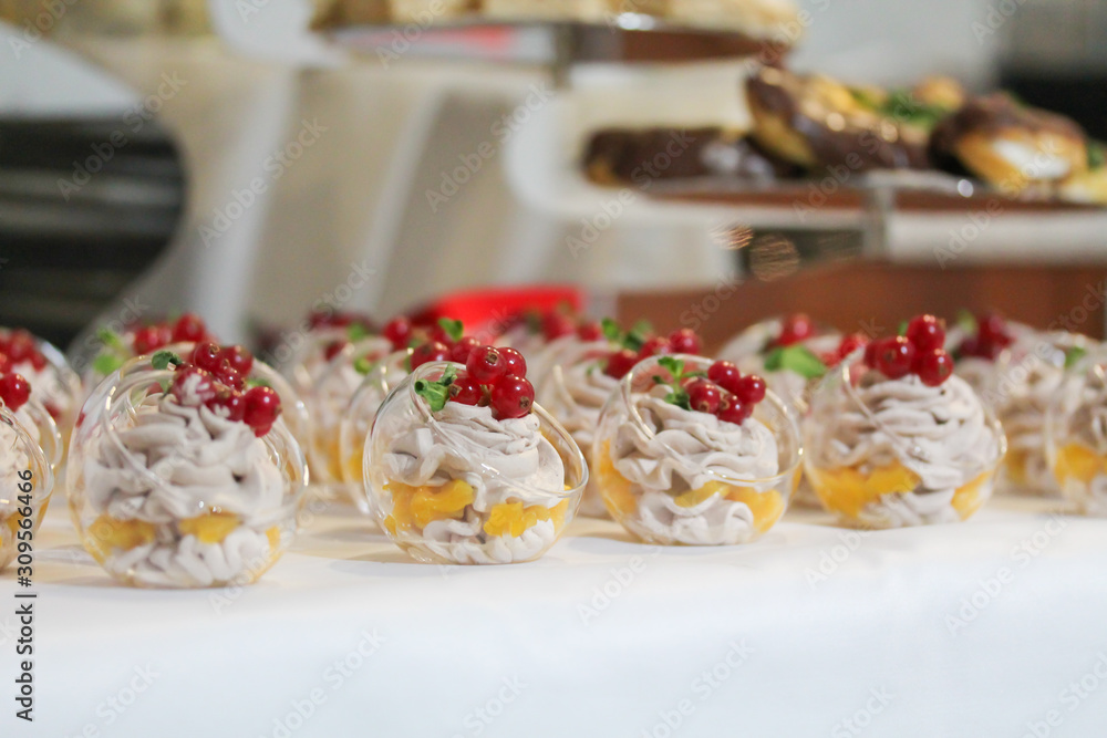 Mini cakes decorated with whipped cream and fresh red currant. Sweet tasty snacks at the party. Food photography. Lots of pastry pieces on the plate. Catering service