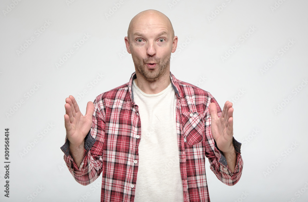 Naklejka premium Shocked bald man showing huge size gesture with hands and looks in surprise with big eyes at the camera.