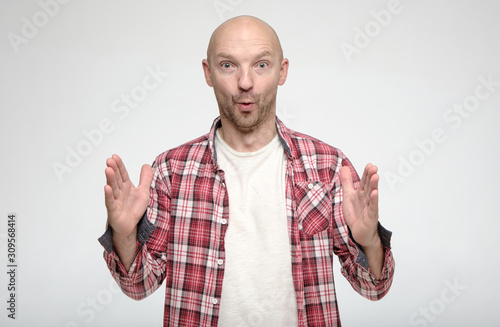 Shocked bald man showing huge size gesture with hands and looks in surprise with big eyes at the camera.