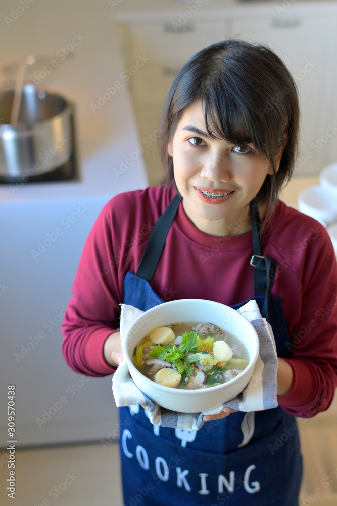 Portrait of smiling young women in modern kitchen and holding a cup of clear Soup with Tofu and Minced Pork. Portrait of smiling young women in modern kitchen and holding a cup of clear Soup with Tofu and Minced Pork.