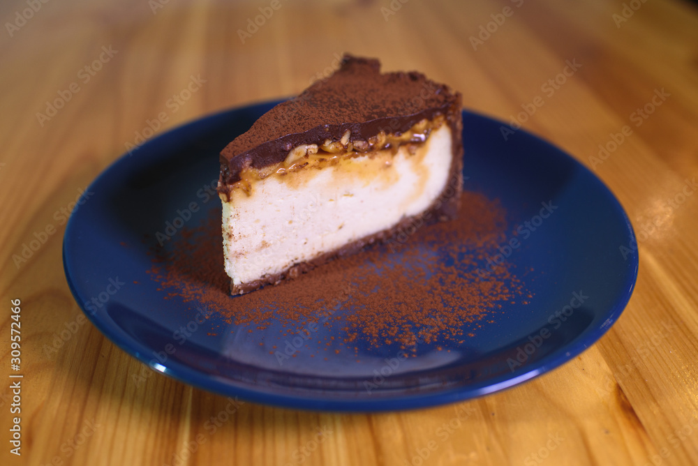 Snickers cheesecake on a blue saucer on a large bright wooden table Snickers cheesecake on a blue saucer on a large bright wooden table