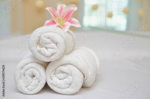 White towel rolls on top with pink Lily flower and Essential oils prepared on massage table for spa treatment