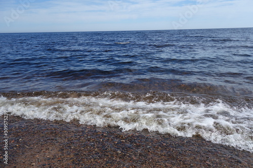 Summer landscape of the lake with clear water, wave, blue sky and horizon.