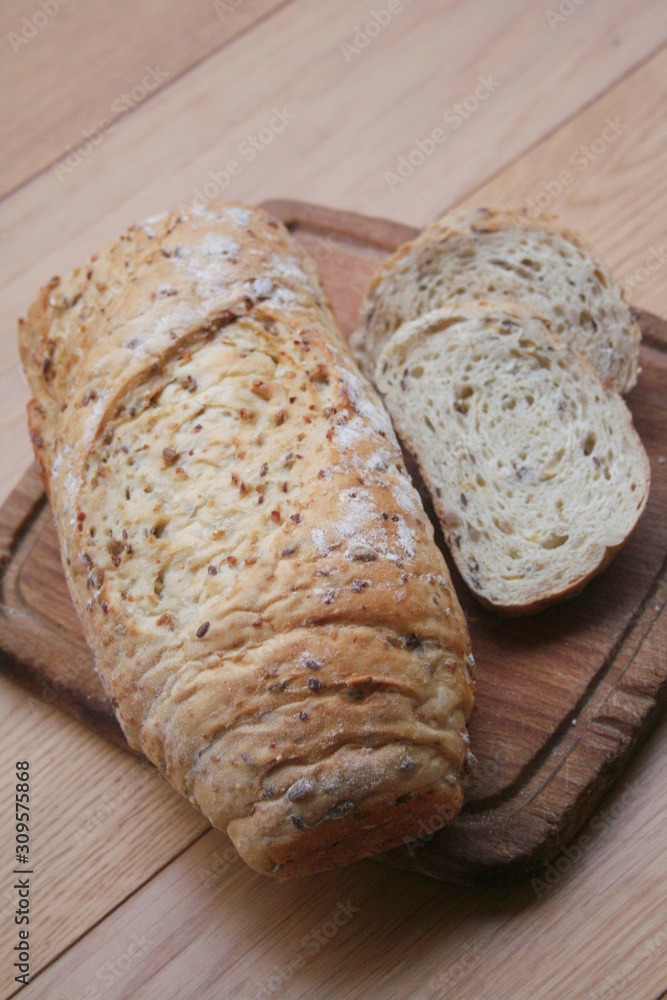 Partially sliced wholegrain organic bread with different seeds on a wooden cutting board on table