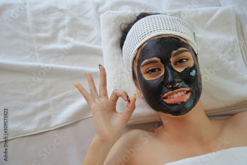 Beautiful young woman relaxing with face mask at beauty spa. Woman getting facial black mud mask at beauty salon.