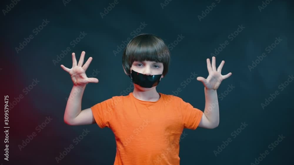 A boy with a sealed mouth shows his palms on a black background. A boy with a sealed mouth shows his palms on a black background.