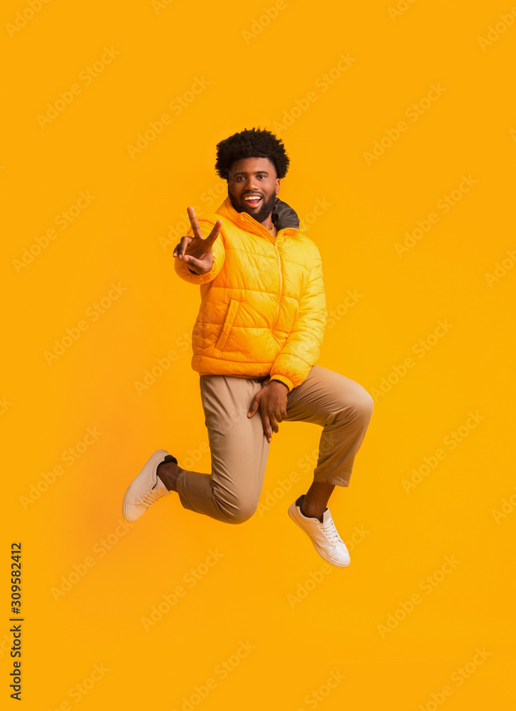 Positive winter black guy greeting with peace gesture while jumping
