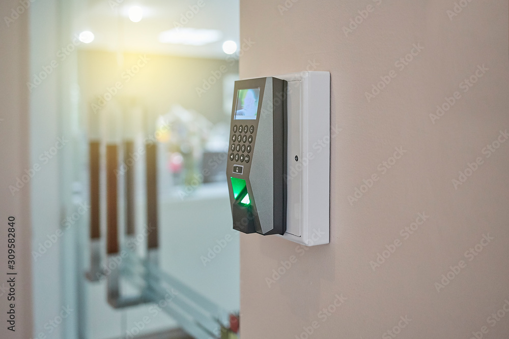 Fingerprint scan machine systems for access interior installed on the wall in front of blur office or co- working space background. Selective Focus. Fingerprint scan machine systems for access interior installed on the wall in front of blur office or co- working space background. Selective Focus.