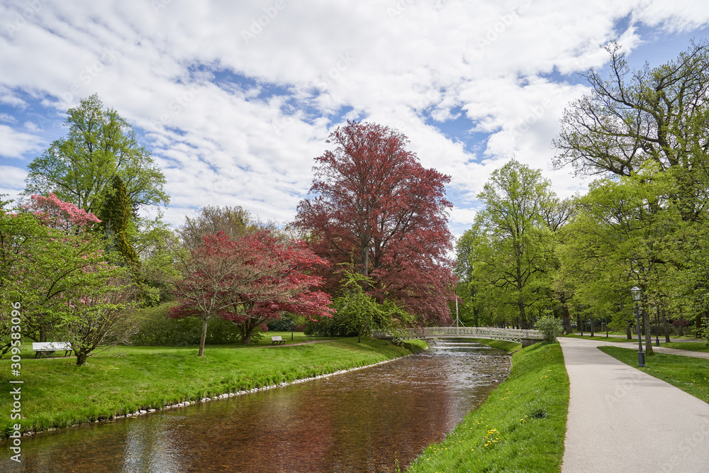 Landscape with a narrow river, trees and an iron bridge and a footpath in a public park in the European city of Baden Baden.