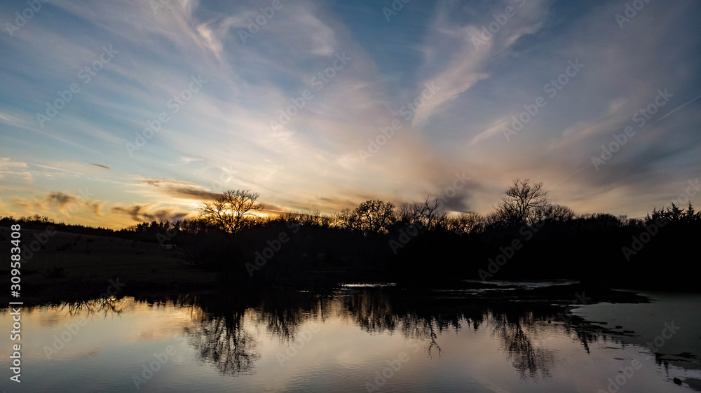 Sunset over rural countryside pond reflecting trees and clouds as ducks and geese swim