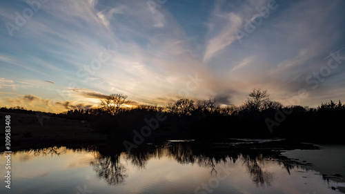 Sunset over rural countryside pond reflecting trees and clouds as ducks and geese swim © Phyre Sky