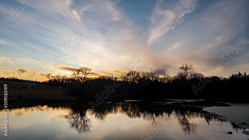 Sunset over rural countryside pond reflecting trees and clouds as ducks and geese swim