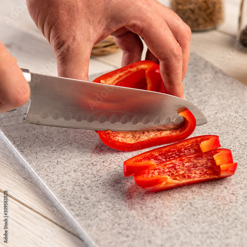 A section of bell pepper with a sharp knife on a cutting board made of artificial stone