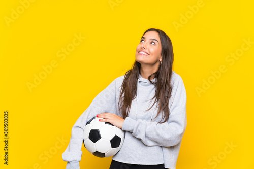 Young football player woman over isolated yellow background looking up while smiling © luismolinero