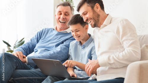 Boy Using Laptop Sitting Between Father And Grandpa At Home