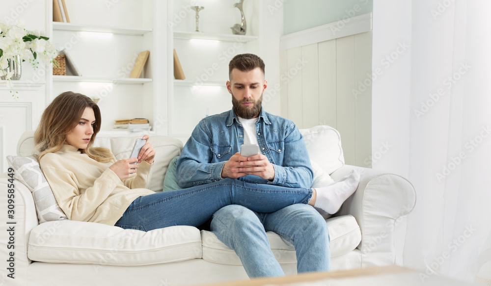 Internet addiction. Young couple using smartphones on sofa