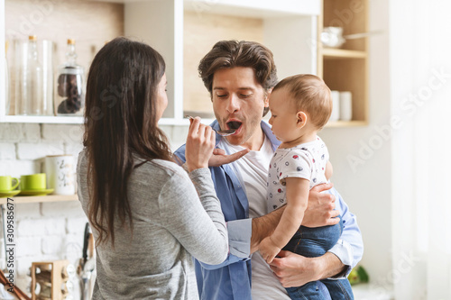 Husband with baby son on hands tasting his wife's meal