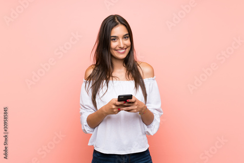 Young woman over isolated pink background sending a message with the mobile