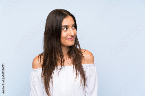 Young woman over isolated blue background standing and looking to the side
