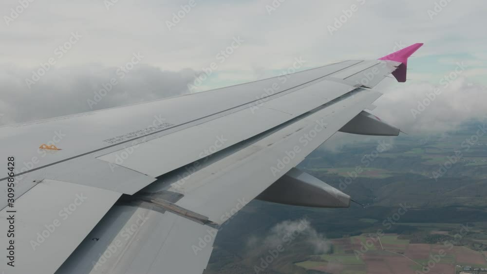 Awesome view from airplane window on fields, woods, green ground. Up in the sky there are white beautiful clouds near plane wing. Part of wing is moving, changing. Awesome view from airplane window on fields, woods, green ground. Up in the sky there are white beautiful clouds near plane wing. Part of wing is moving, changing.