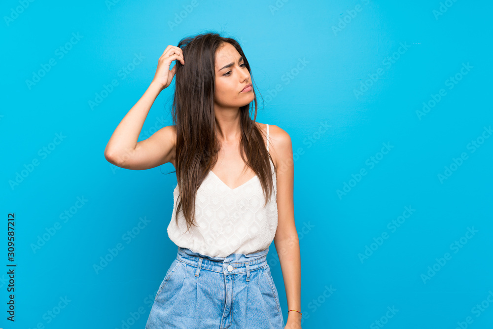 Young woman over isolated blue background having doubts while scratching head Young woman over isolated blue background having doubts while scratching head