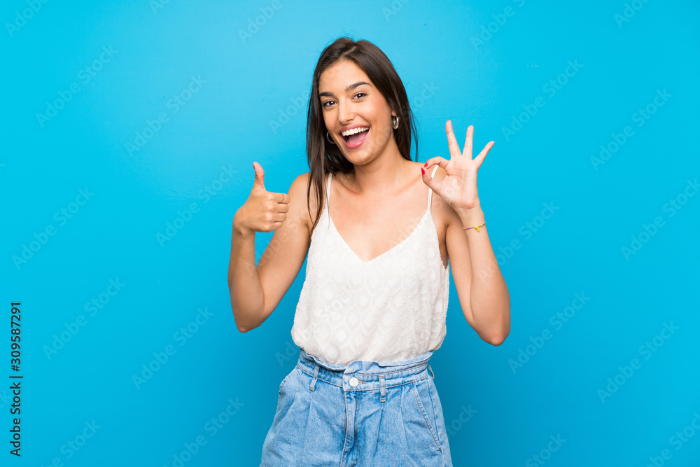 Young woman over isolated blue background showing ok sign and thumb up gesture Young woman over isolated blue background showing ok sign and thumb up gesture