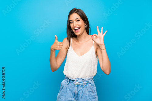 Young woman over isolated blue background showing ok sign and thumb up gesture