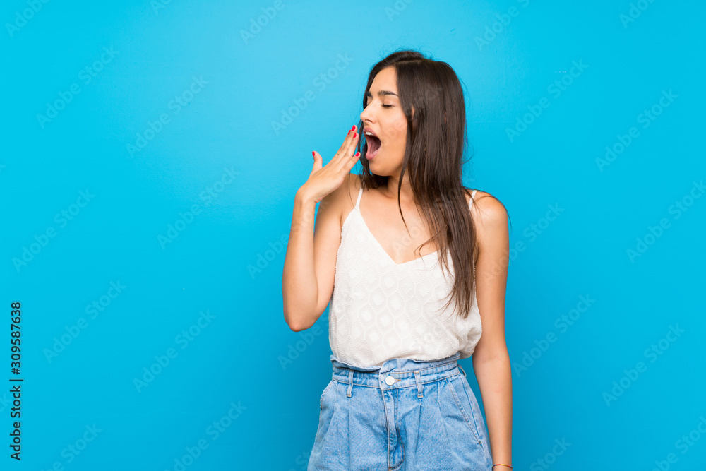 Young woman over isolated blue background yawning and covering wide open mouth with hand Young woman over isolated blue background yawning and covering wide open mouth with hand