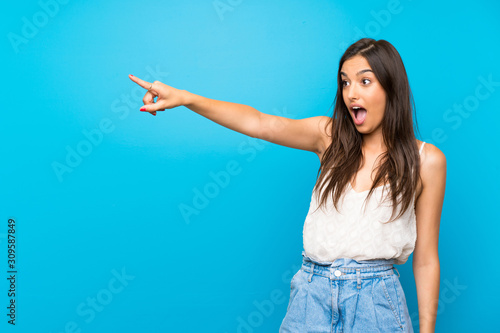 Young woman over isolated blue background pointing away