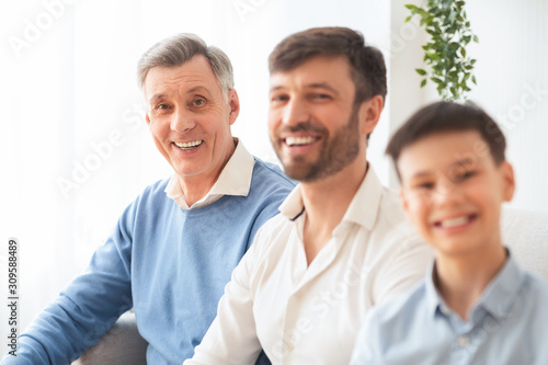 Elderly Man With Middle-Aged Son And Grandson Sitting On Couch