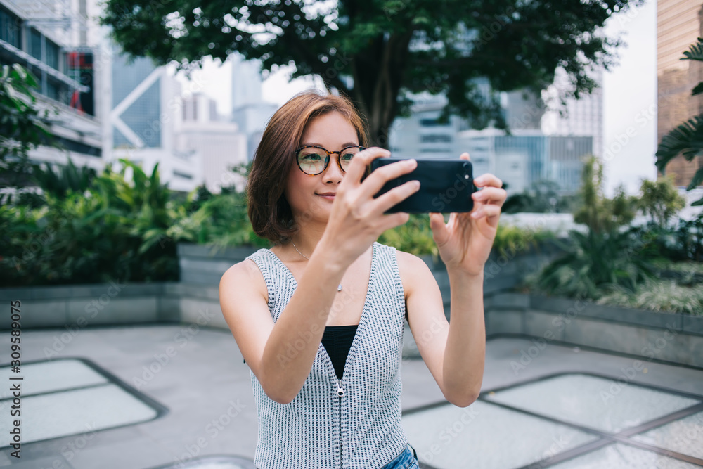 Cheerful adult pretty female in casual wear and eyeglasses capturing selfie on city street Cheerful adult pretty female in casual wear and eyeglasses capturing selfie on city street