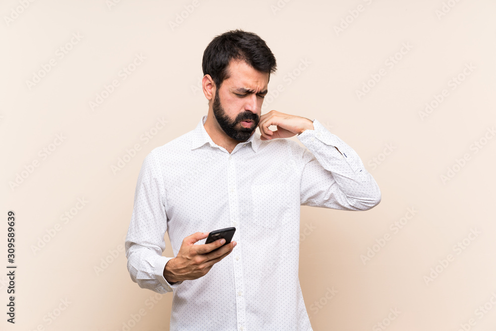 Young man with beard holding a mobile with tired and sick expression Young man with beard holding a mobile with tired and sick expression
