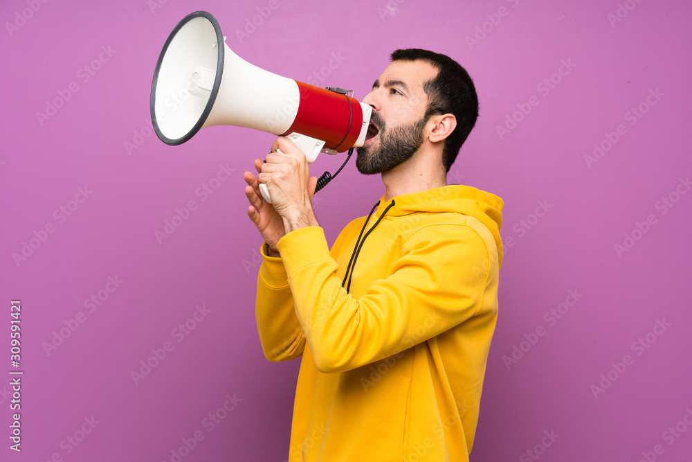 Handsome man with yellow sweatshirt shouting through a megaphone Handsome man with yellow sweatshirt shouting through a megaphone