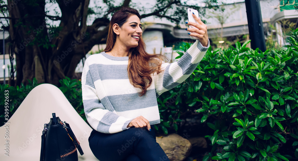 Naklejka premium Happy modern woman taking selfie with smartphone on street