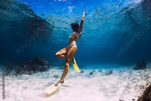 Free diver young girl with yellow fins glides over sandy bottom and corals.