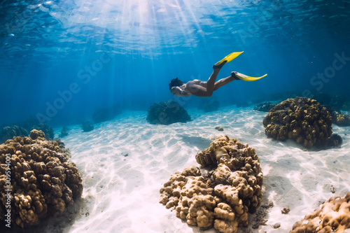 Free diver young girl with yellow fins glides over sandy bottom and corals.