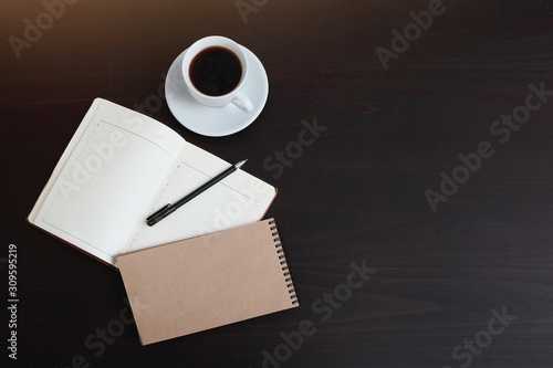 Spiral notebook and organizer on a dark table with a Cup of coffee. The view from the top. Copy space. Sunlight.