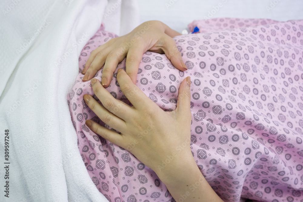 Pregnant woman lying in bed in hospital room and touching her belly for feeling her new baby. Pregnancy, motherhood, hope, expectation concept background. Mother candidate waiting for birth operation. Pregnant woman lying in bed in hospital room and touching her belly for feeling her new baby. Pregnancy, motherhood, hope, expectation concept background. Mother candidate waiting for birth operation.