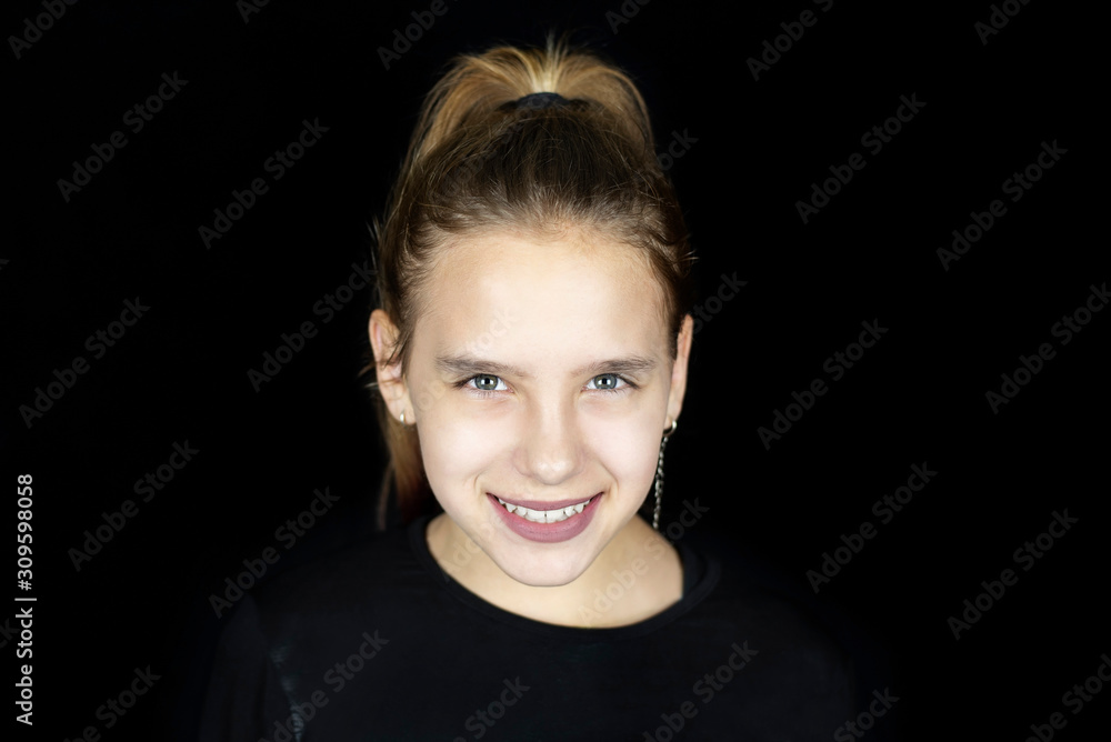 Fototapeta premium Beautiful young girl is sincerely smiling on a dark background, she has a beautiful smile because she wore braces on her teeth
