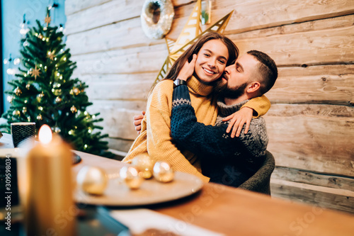 Obraz na plátně Joyful couple sitting at decorated new year table and cuddling