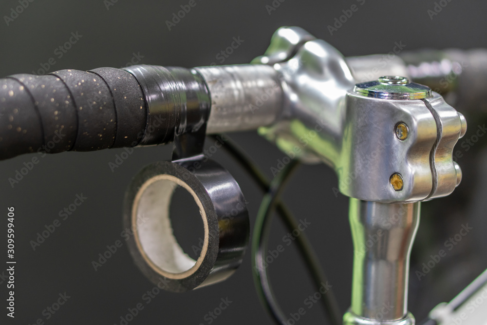 Road bike handlebars on a black background. Install handlebar tape black. Bicycle repair in a modern workshop. Black insulating tape close-up. Road bike handlebars on a black background. Install handlebar tape black. Bicycle repair in a modern workshop. Black insulating tape close-up.