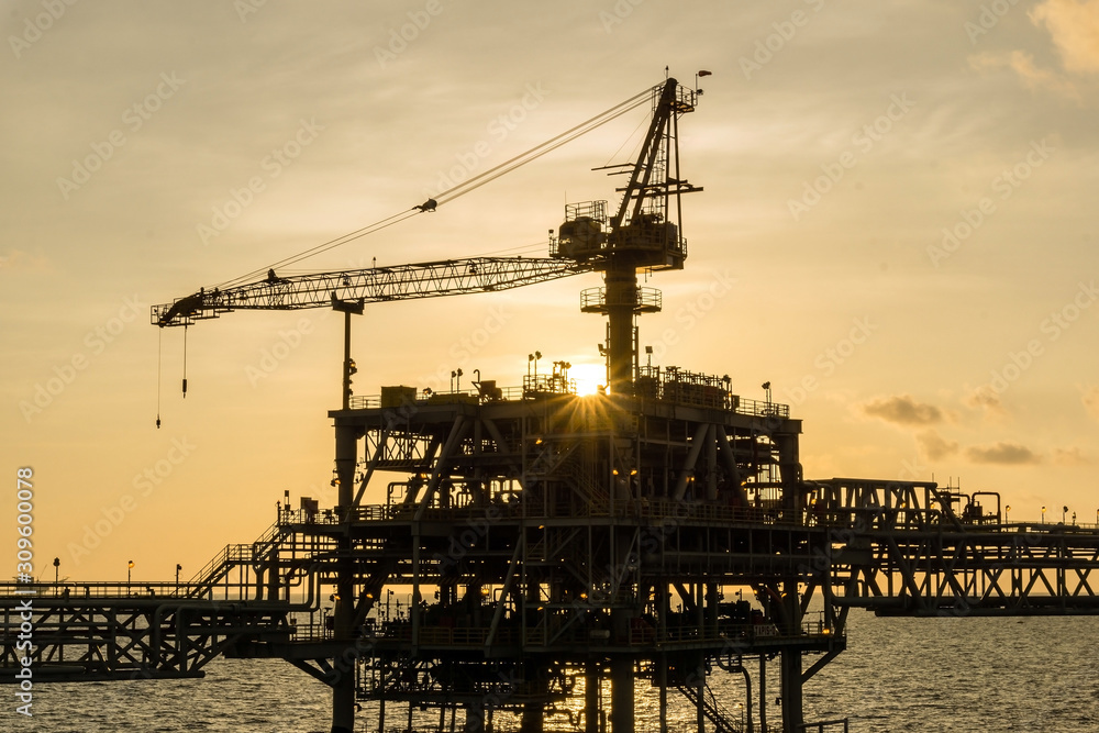 Silhouette of a crane on an oil production platform at oil field during sunset Silhouette of a crane on an oil production platform at oil field during sunset