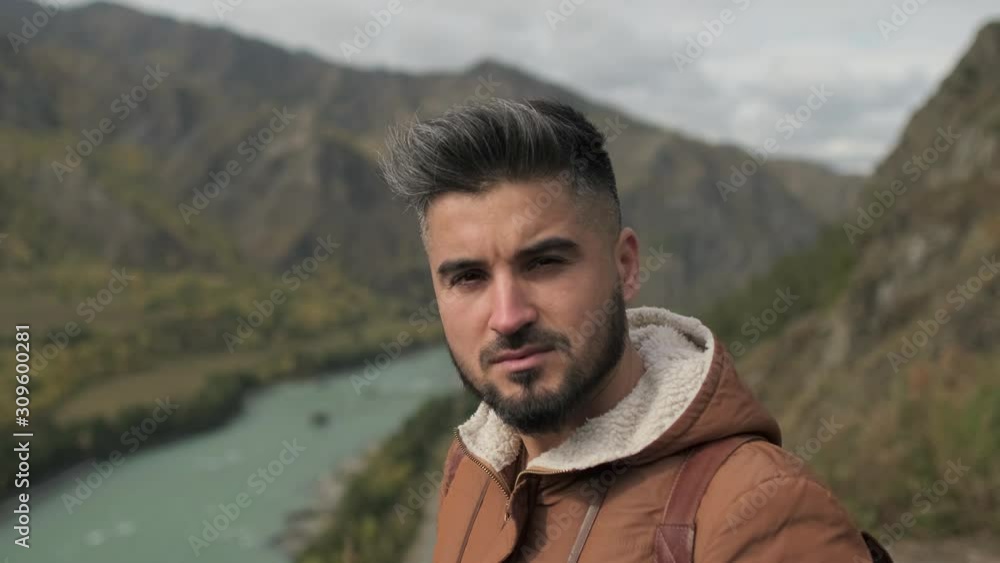 Portrait of bearded attractive young hiker tourist traveler man looking at camera, traveling on mountain, Active lifestyle hiking vacation travel tourism adventure summer landscape nature. 4 K slow-mo Portrait of bearded attractive young hiker tourist traveler man looking at camera, traveling on mountain, Active lifestyle hiking vacation travel tourism adventure summer landscape nature. 4 K slow-mo