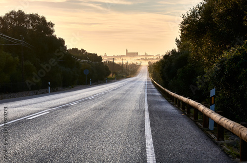 Road and in the background Mallorcan village among fog. Mediterranean people. Church silhouette Santanyi, Mallorca